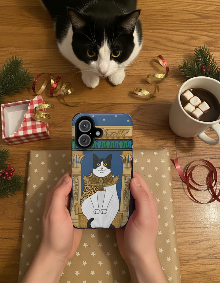 Styled scene: hands hold a phone case printed with an AI-rendered, Egyptian-style portrait of a black-and-white cat over gift wrap, the same cat watching